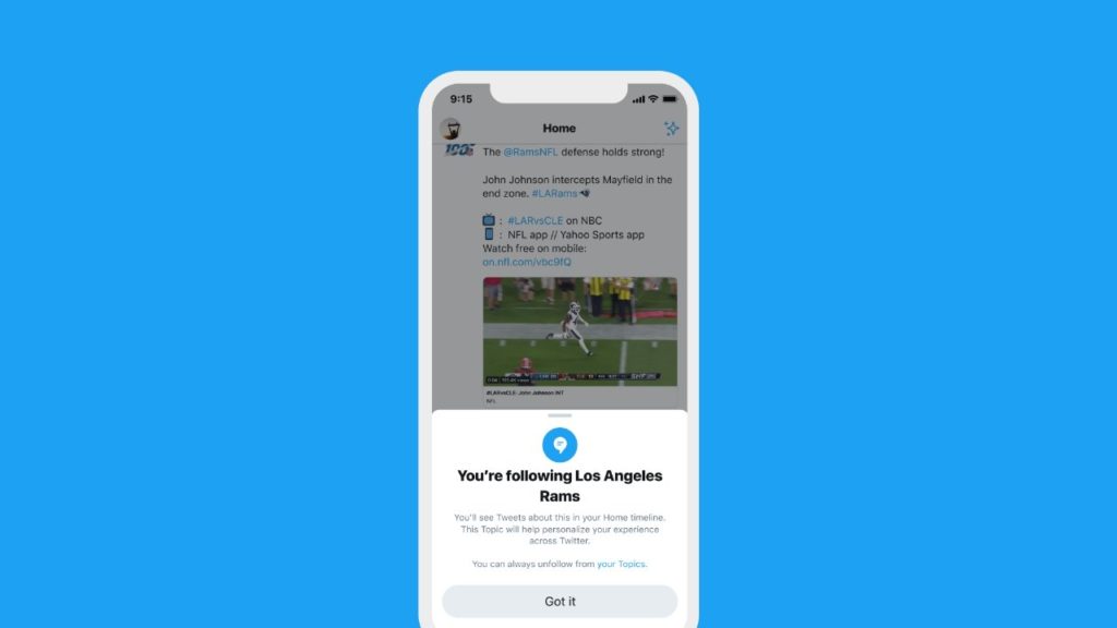 Image of a phone showing the Twitter interface darkened in the back with an announcement at the bottom saying ‘ You’re following Los Angeles Rams’ - You'll see tweets about them in your Home timeline. This Topic will help personalise your experience accross Twitter; You can always unfollow from ‘your Topics’’ 